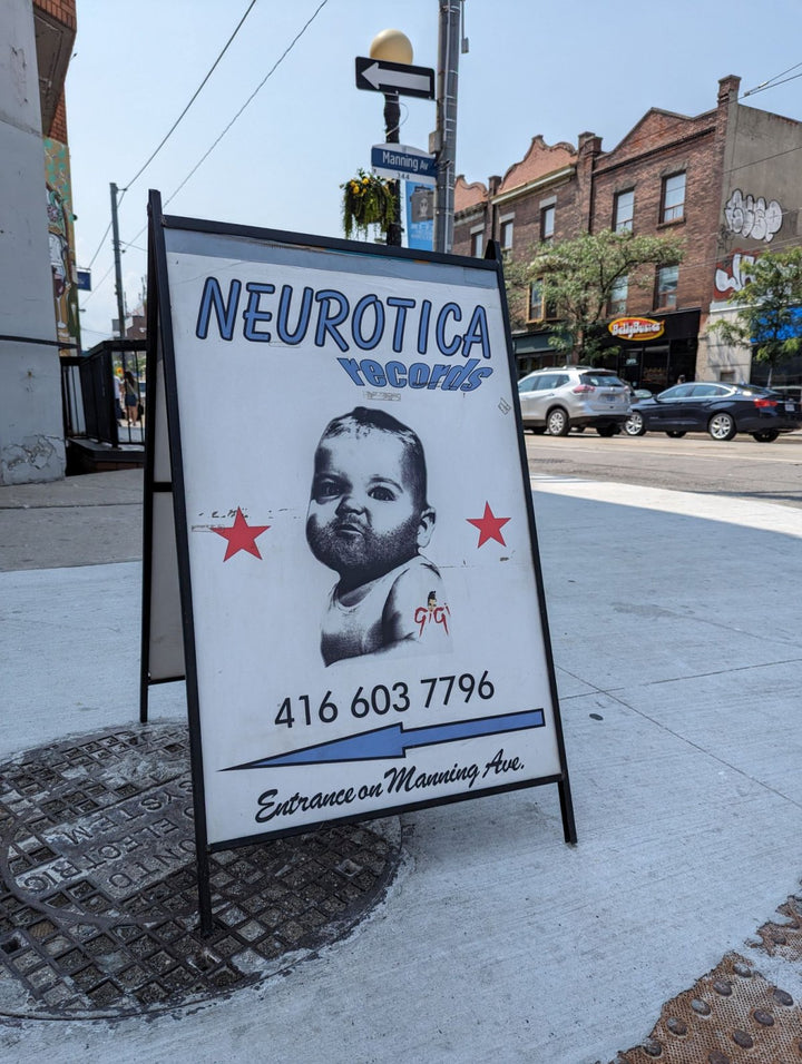 Neurotica Records sidewalk sign directing visitors to the Manning Avenue entrance at 567 College Street in Toronto.